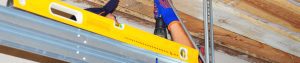 A man installing metal tracks in a garage. A level rests on the horizontal part of the standard lift track.