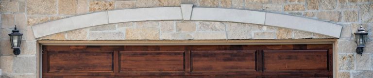 A white brick home has a closed wooden garage door with a pattern of brown rectangular slats and panels.