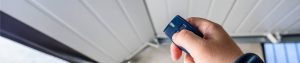 A man's hand reaching out with a garage door remote and clicking the button toward a folding white garage door.