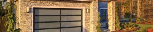 A stone home with a tailored front yard and a garage door with frosted glass windows. Warm light is cast over the house.